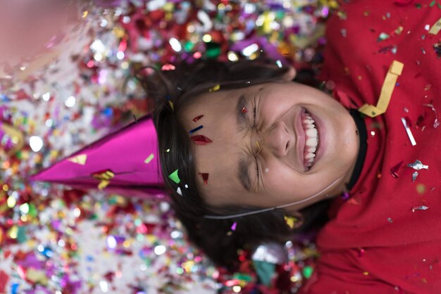 Heureux enfant célébrant la fête avec des confettis soufflants en position allongée sur le sol