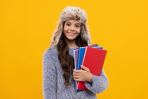 Heureux enfant cheveux longs en chapeau avec cahier sur fond jaune éducation