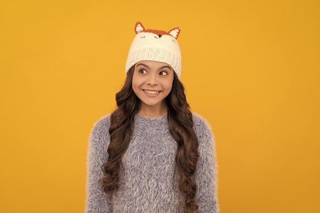 Heureux enfant cheveux longs en chapeau sur fond jaune hiver