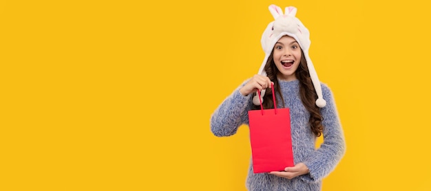 Heureux enfant cheveux longs en chapeau tenir pack sur fond jaune nouvel an bannière de shopping enfant fille studio affiche en-tête avec copie espace