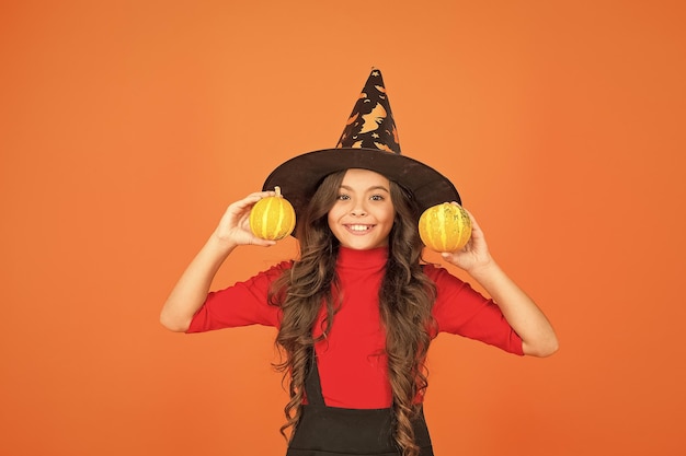 Heureux enfant en costume de chapeau de sorcière à halloween avec une petite nourriture d'halloween à la citrouille jaune