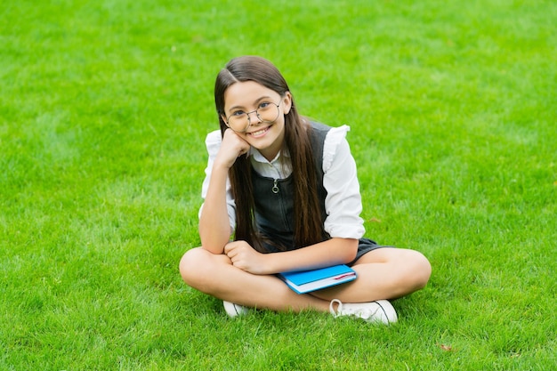 Heureux enfant dans des verres assis sur l'herbe verte avec un livre