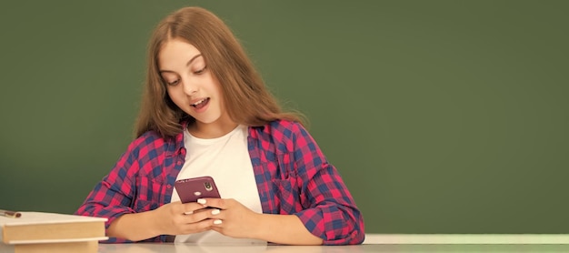 Heureux enfant discutant sur smartphone dans la salle de classe au message du tableau noir Affiche isolée horizontale d'une étudiante de l'école Bannière en-tête portrait d'écolière copie espace