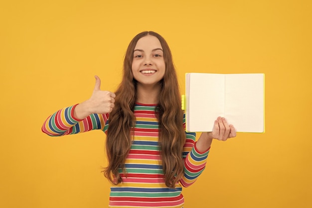 Heureux enfant donner le pouce en l'air geste de la main tenant un livre ouvert pour copier l'espace fond jaune satisfait