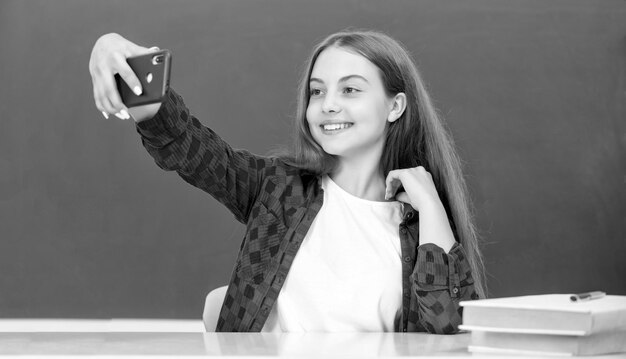 Heureux enfant faisant selfie sur smartphone en classe au portrait de tableau noir