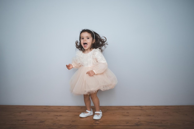 Heureux Enfant Fille 2-3 Ans Vêtue D'une Robe De Princesse Dans La Chambre  Se Bouchent. En Regardant La Caméra. Enfance. Fête D'anniversaire. Joie.