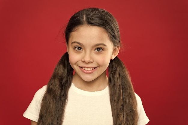 Heureux enfant fille aux cheveux longs sur fond rouge Bonheur et joie Émotions positives Garde d'enfants et éducation Enfant souriant visage mignon vivre une vie heureuse insouciante Profiter de chaque instant Jeune et libre