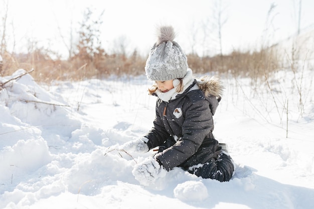 Heureux enfant fille jouant sur une promenade d'hiver enneigée portant des salopettes de neige noire cool tenue d'hiver