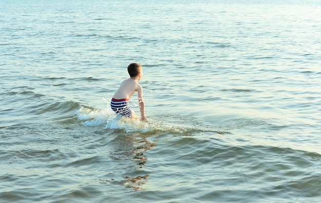 Heureux enfant garçon court joyeusement pour nager dans la mer Concept d'été et de voyage