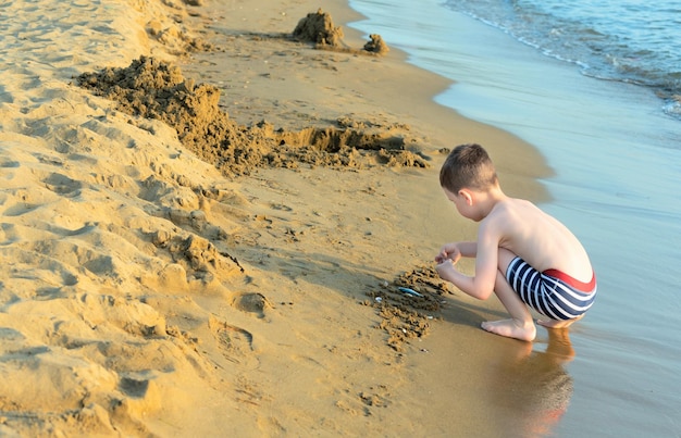 Heureux enfant garçon jouant avec du sable au bord de la mer Concept d'été et de voyage