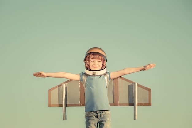 Heureux enfant jouant avec des ailes de jouet sur fond de ciel d'été. Rétro tonique