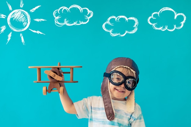 Heureux enfant jouant avec un avion en bois vintage contre le mur bleu.