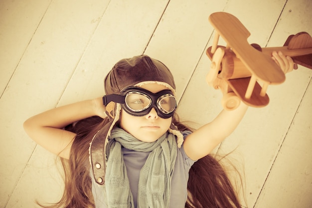 Photo heureux enfant jouant avec un avion jouet. enfant allongé sur le plancher en bois à la maison. rétro tonique