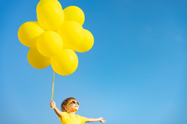 Heureux enfant jouant avec des ballons jaunes en plein air. Enfant s'amusant sur fond bleu ciel d'été. Concept de liberté et de mode de vie actif