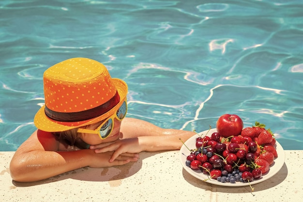 Heureux enfant jouant dans la piscine Vacances d'été pour les enfants Fruits d'été pour les enfants Petit garçon se relaxant dans une piscine s'amusant pendant les vacances d'été