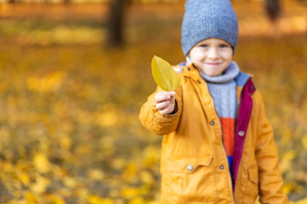 Heureux enfant jouant avec des feuilles jaunes tombées lors d'une promenade à l'automne dans le parc.