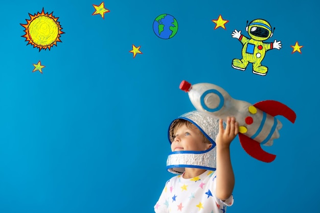 Heureux enfant jouant avec une fusée jouet sur fond bleu. Kid prétend être astronaute. Imagination et concept de rêve d'enfants