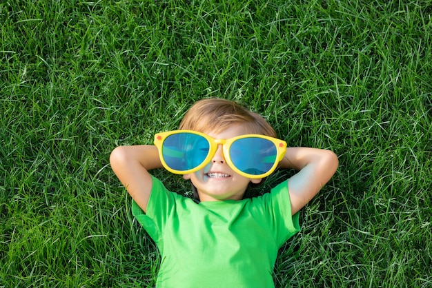 Heureux enfant jouant en plein air dans le parc du printemps. Enfant allongé sur l'herbe verte. Jour de la Terre et concept d'écologie. Vue de dessus portrait de garçon à l'extérieur