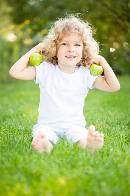 Heureux enfant jouant avec des pommes sur l'herbe verte dans le parc du printemps