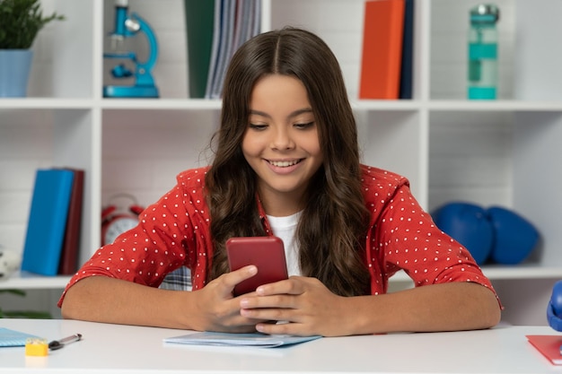 Heureux enfant longs cheveux bouclés textos sur smartphone dans le message de la classe