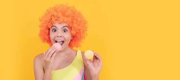 Heureux enfant en maillot de bain portant une perruque frisée orange mangeant des cheveux macaron français Adolescent enfant avec des bonbons affiche bannière en-tête copie espace