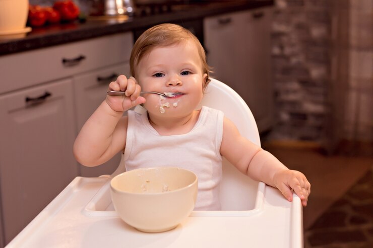Photo heureux enfant de manger de la bouillie de lait avec une cuillère, fille assise sur une chaise d'alimentation dans la cuisine