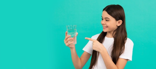 Heureux enfant pointant le doigt sur un verre d'eau pour maintenir l'équilibre quotidien de l'eau dans le corps Bannière d'enfant fille avec verre d'eau portrait en studio avec espace de copie