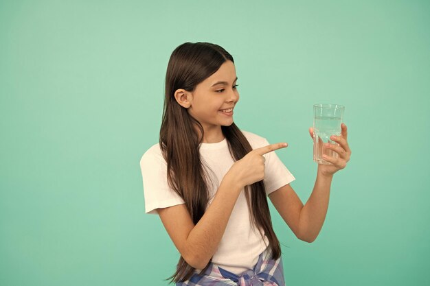 Heureux enfant pointant le doigt sur un verre d'eau pour maintenir l'équilibre quotidien de l'eau dans l'hydratation du corps