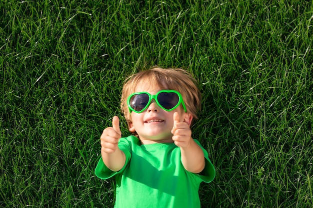 Heureux enfant portant sur l'herbe verte. Funny kid en plein air dans le jardin de printemps. Jour de la terre et concept de mode de vie sain