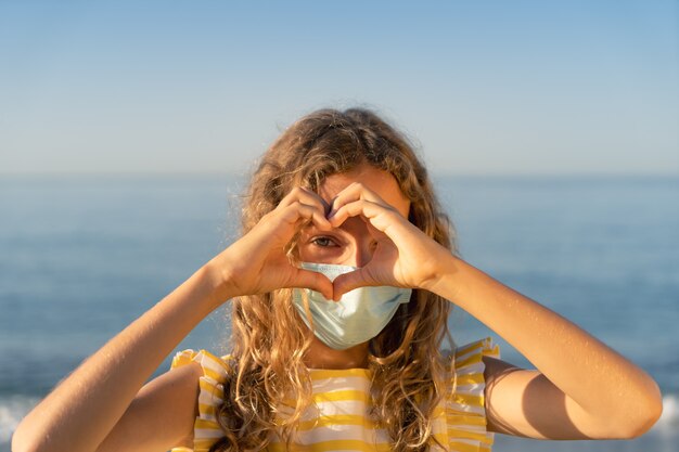 Heureux enfant portant un masque médical en plein air contre le ciel bleu.