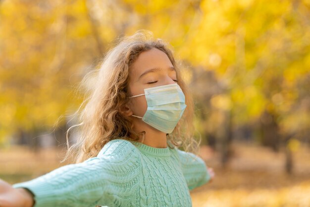 Heureux enfant portant un masque de protection en plein air dans un parc à l'automne.