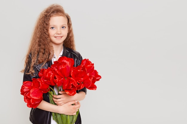 Heureux enfant portant une veste en cuir embrassant un grand bouquet de tulipes, regardant à l'avant avec le sourire