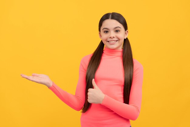 Heureux enfant présentant le produit sur l'espace de copie sur fond jaune pouce vers le haut