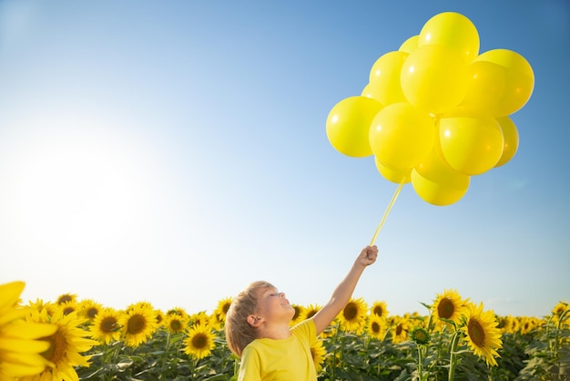 Heureux enfant s'amusant au printemps champ de tournesols Portrait en plein air d'enfant avec des ballons colorés sur fond de ciel bleu