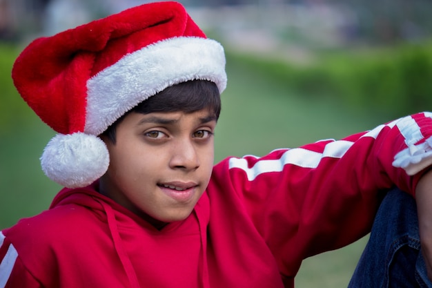 Un heureux enfant souriant attrayant en casquette de père Noël, regardant la caméra joyeusement