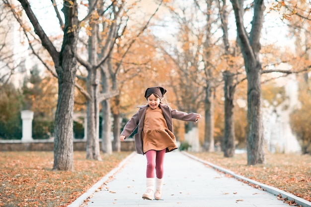 Heureux enfant souriant porter une veste et un chapeau dans le parc avec des feuilles mortes sur fond de nature Automne