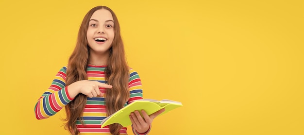 Heureux enfant sourire pointant du doigt au livre scolaire étude de fond jaune bannière d'écolière étudiant écolier élève portrait avec copie espace