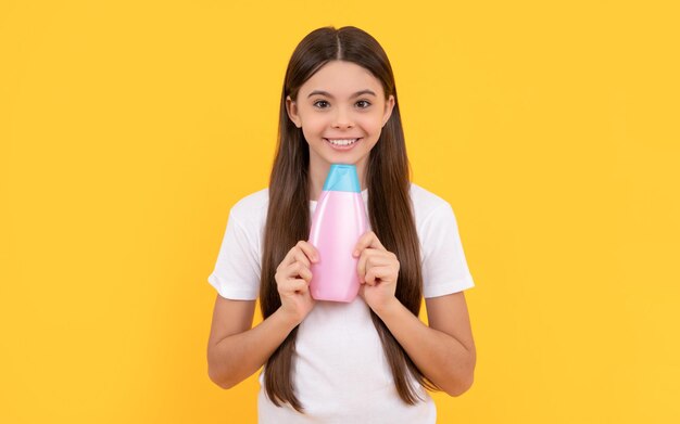 Heureux enfant tenant une bouteille de shampoing sur fond jaune cosmétique