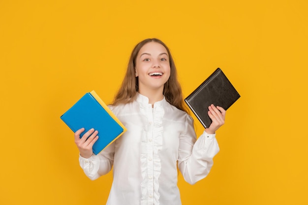 Heureux enfant tenant des devoirs scolaires sur fond jaune, retour à l'école.