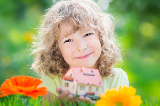 Heureux enfant tenant la maison dans les mains sur fond vert printemps Concept d'entreprise immobilière