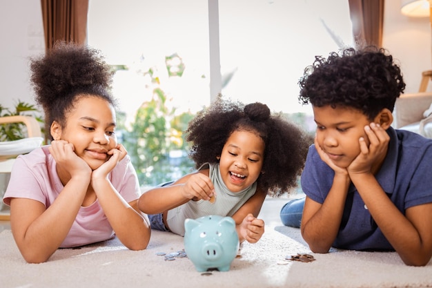 Heureux les enfants afro-américains économiser de l'argent dans une tirelire ensemble dans le salon à la maison