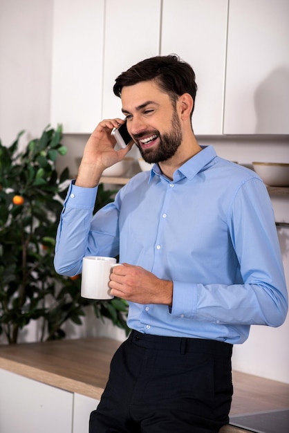 Heureux d'entendre un bel homme d'affaires joyeux parler au téléphone tout en buvant du thé dans la cuisine