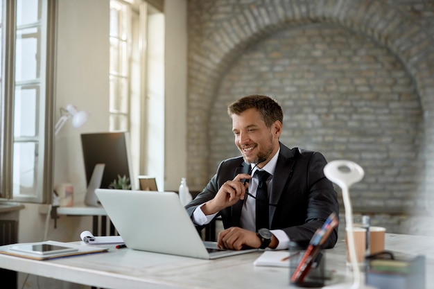 Heureux entrepreneur d'âge moyen surfant sur le net sur un ordinateur au bureau