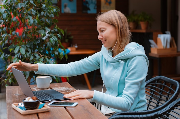 Heureux entrepreneur travaillant avec un téléphone et un ordinateur portable dans un café dans la rue