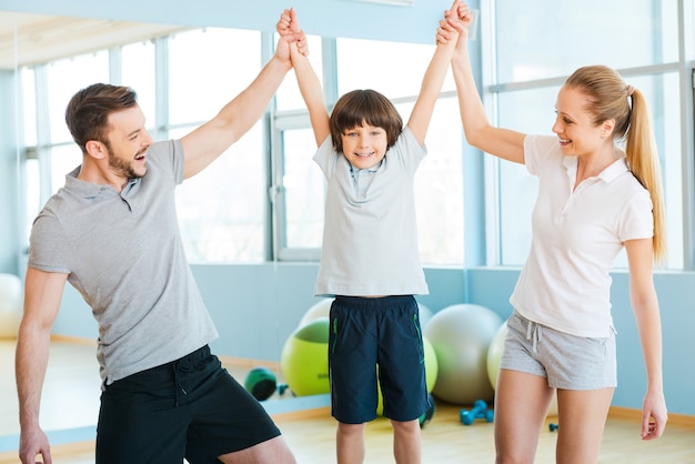 Heureux d'être en bonne santé. Heureux père et mère s'amusant avec leur fils dans un club de remise en forme avec des balles de fitness posées en arrière-plan