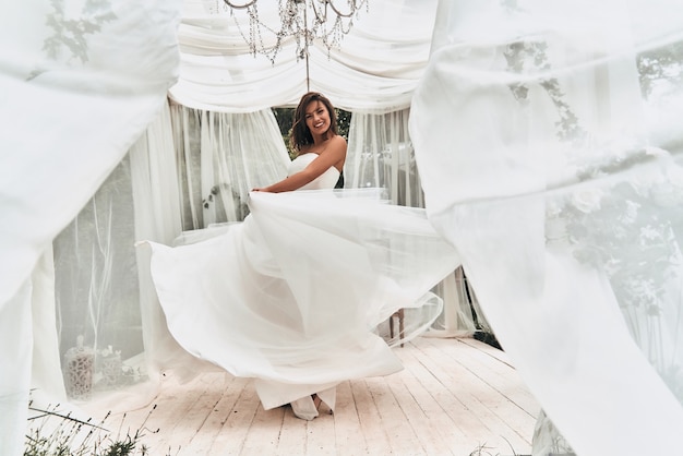 Heureux d'être marié. Toute la longueur d'une jeune femme séduisante en robe de mariée souriante en dansant dans le pavillon de mariage à l'extérieur