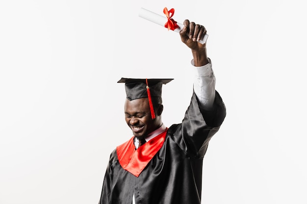 Heureux étudiant africain en robe de graduation noire et casquette lève le diplôme de maîtrise au-dessus de la tête sur fond blanc Un homme africain diplômé est diplômé de l'université et célèbre la réussite scolaire