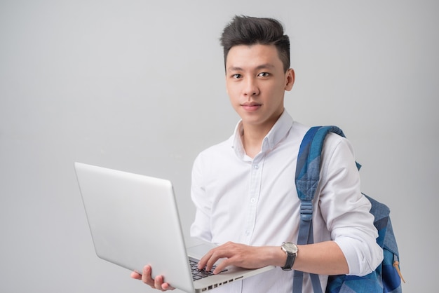 Heureux étudiant asiatique décontracté utilisant un ordinateur portable isolé sur fond gris