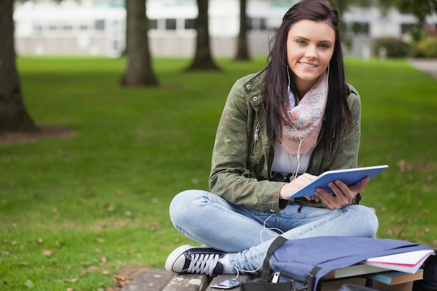 Heureux étudiant brune à l&#39;aide de tablette assis sur un banc