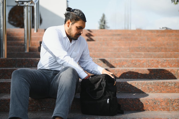 Heureux étudiant indien assis sur les escaliers du campus universitaire